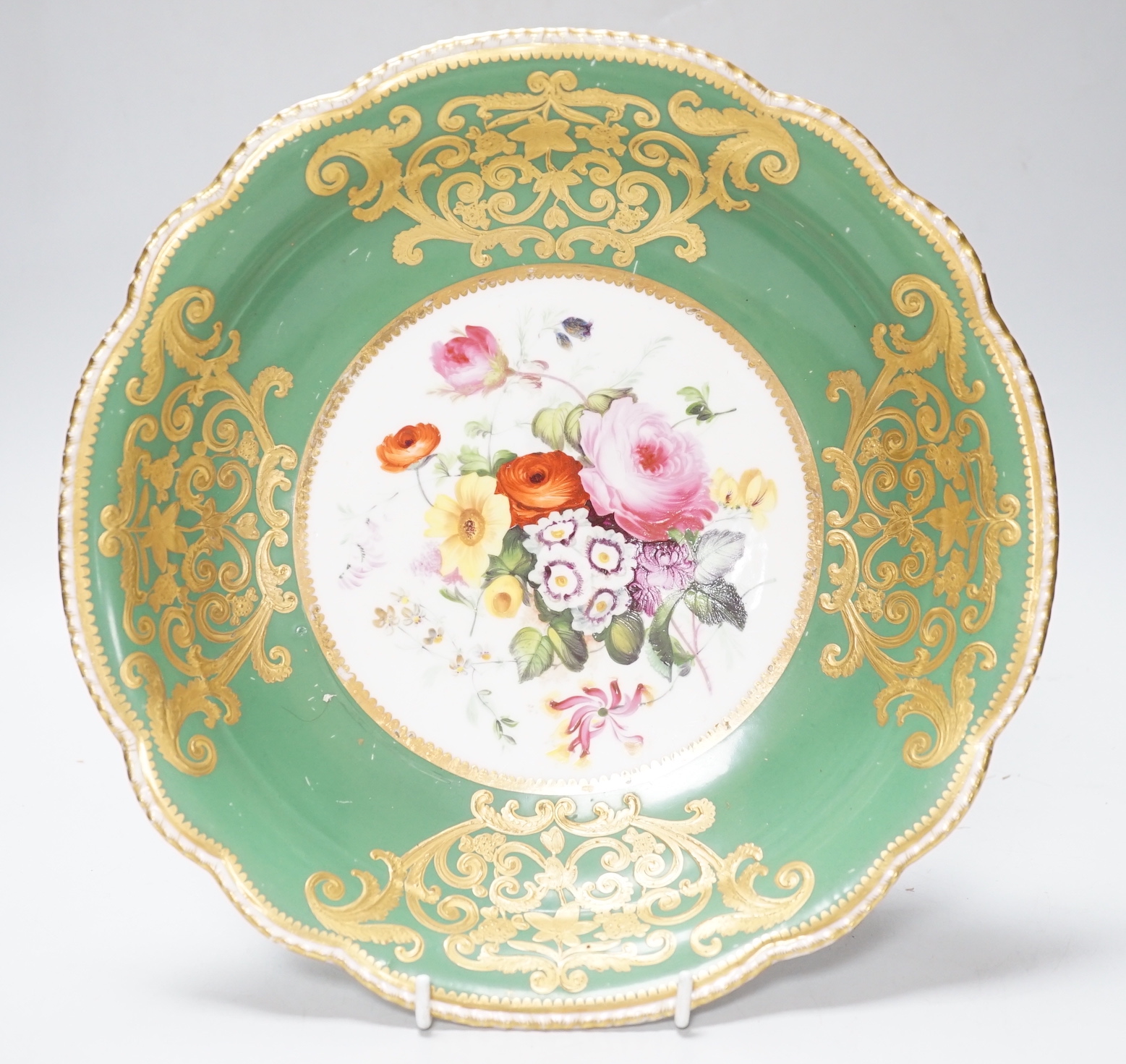 An English porcelain large bowl the centre painted with a bouquet of flowers under a green border with four ornately gilded designs, c.1820, 28cms diameter